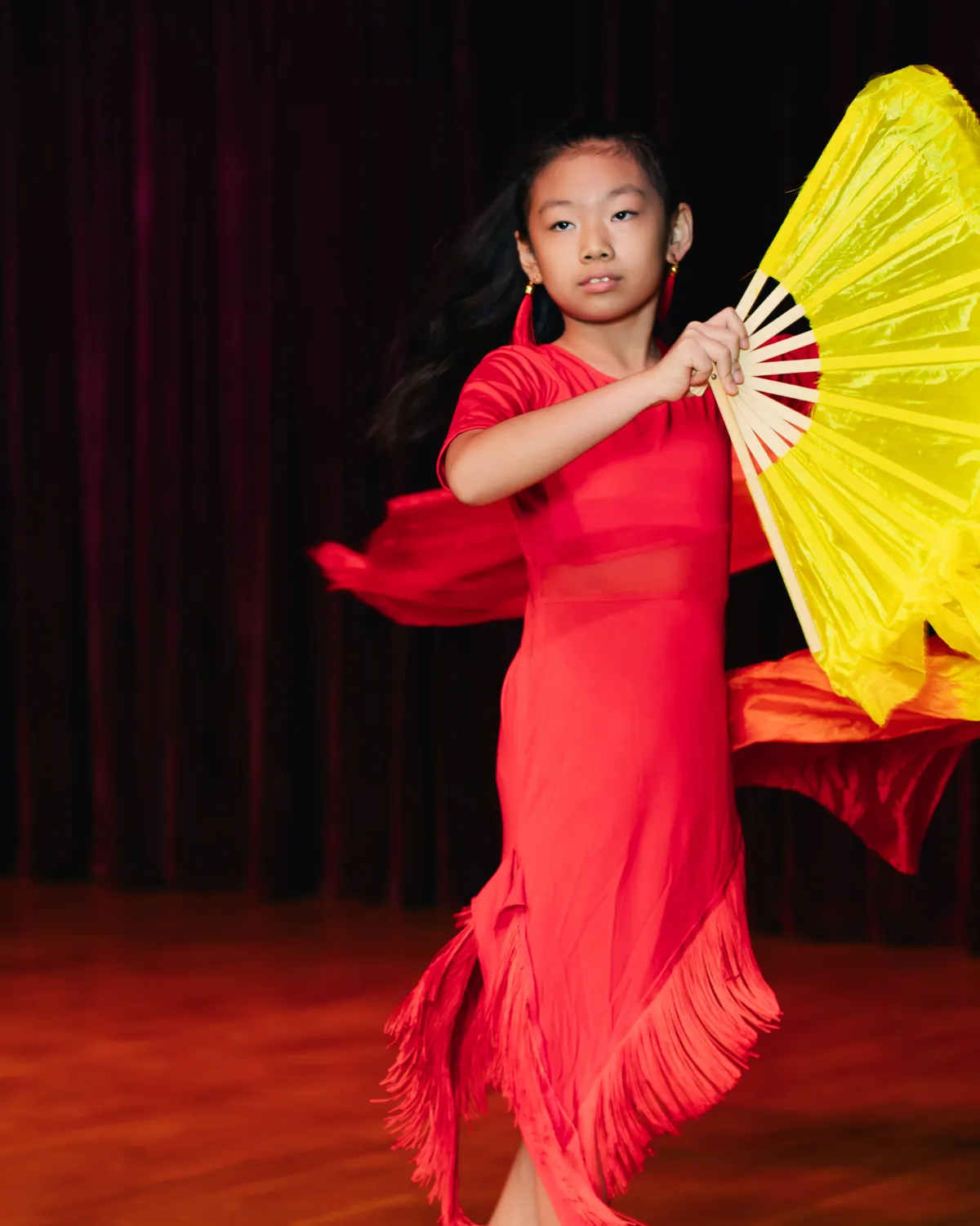 A young dancer performing a fan routine on stage